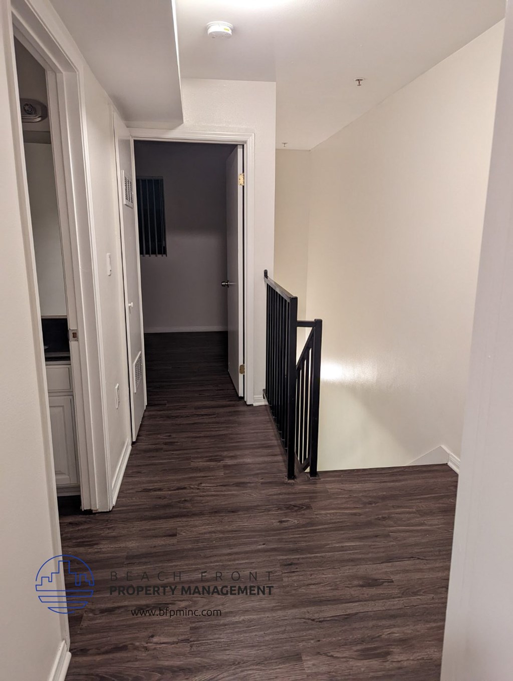 a hallway with white walls and wood flooring and a hallway leading to a door